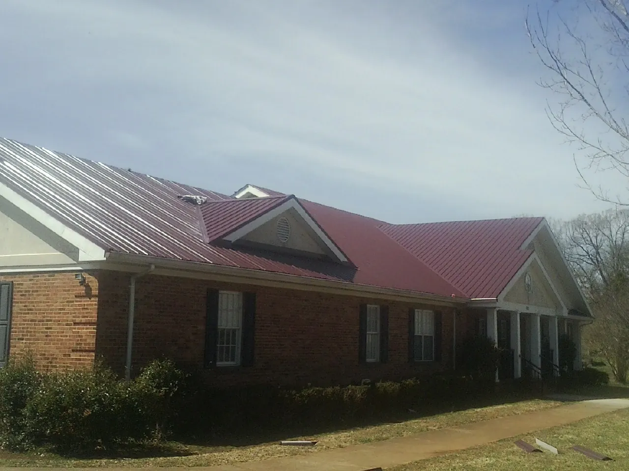 Red metal roof with gabled entries on a long brick building, from a Hail Damage Roof Repair job in Texarkana