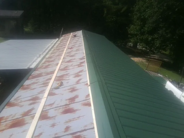 Old rusted panels beside newly installed green metal roofing — Wind Damage Roof Repair by Roofing Brothers in Texarkana
