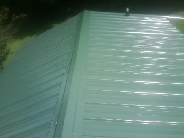 New green metal panels meeting at the ridge of a roof — Flat Roof Repair work by our crew in Texarkana