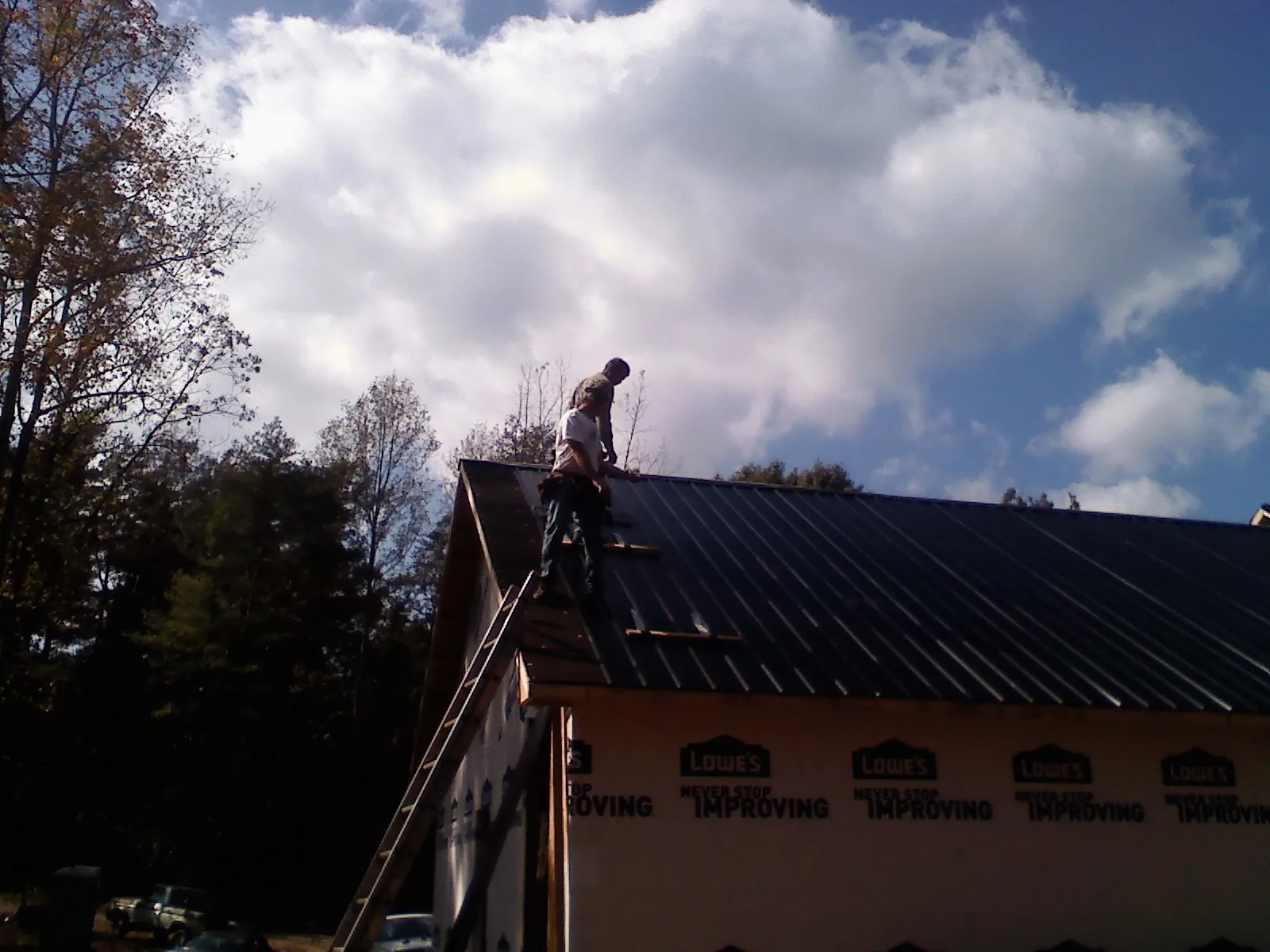 Roofer fastening dark metal panels high against a cloudy sky, from a Roof Inspection job in Texarkana