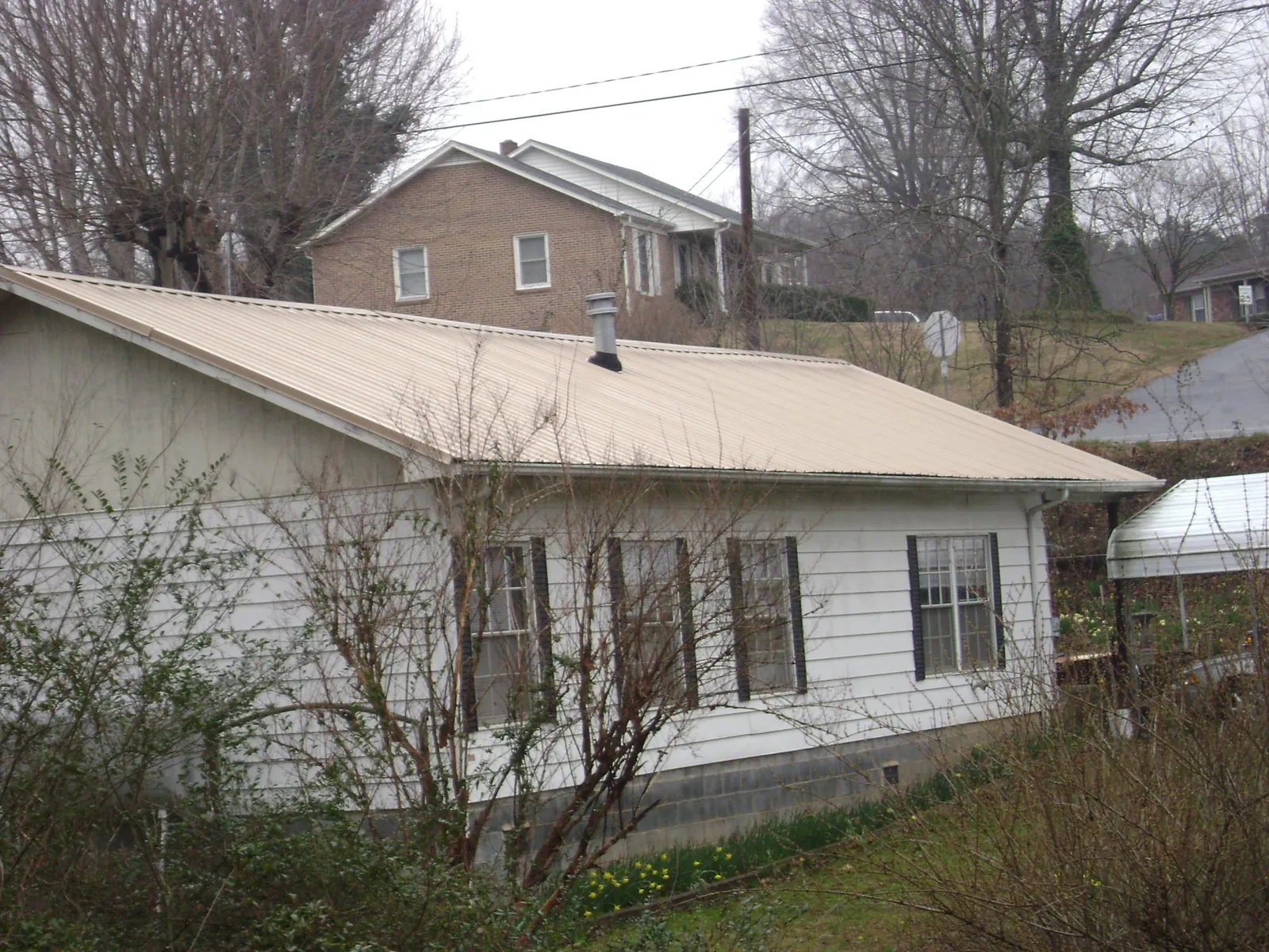 Tan metal roof on a white sided house set into a hillside — Commercial Roofing by Roofing Brothers in Texarkana